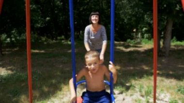 Mutlu çocuk oğlu Street Swing Bahçesi ağır çekimde, üzerinde sallanan anne