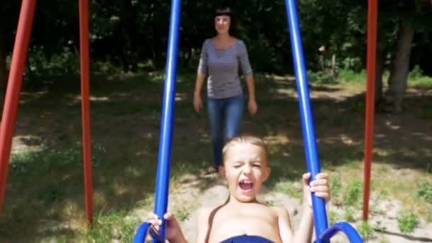 Mãe balançando seu menino feliz em um balanço de rua no parque infantil em câmera lenta — Vídeo de Stock