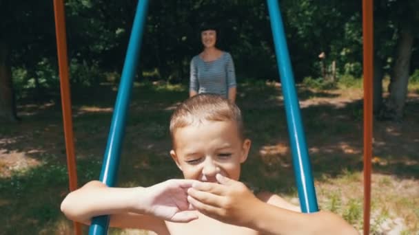 Mãe balançando seu menino feliz em um balanço de rua no parque infantil em câmera lenta — Vídeo de Stock