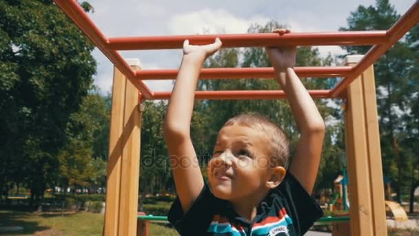 Jonge jongen hangen Monkey Bars door zijn handen te oefenen op de speelplaats tegen de hemel in Slow Motion — Stockvideo