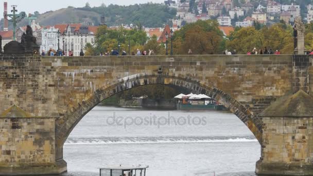 Menschen spazieren über die alte Prager Brücke und das auf der Vitava schwimmende Boot — Stockvideo