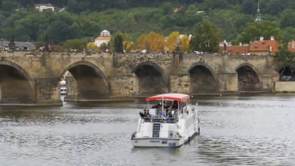 Άνθρωποι περπατούν κατά μήκος του παλιά γέφυρα της Πράγας και η βάρκα επιπλέει στον ποταμό Μολδάβα — Αρχείο Βίντεο