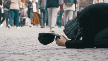 Kaldırımda şapkalı evsiz dilenci adam sadaka üzerinden geçen insanlar için yalvarır. Ağır çekim