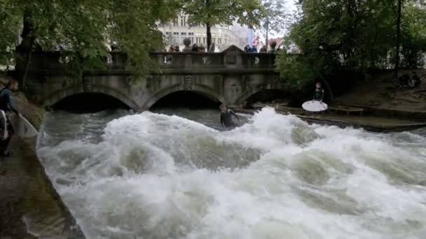 Αστική surfers βόλτα το κύμα στέκεται στις όχθες του ποταμού Eisbach, Μόναχο, Γερμανία. Αργή κίνηση — Αρχείο Βίντεο