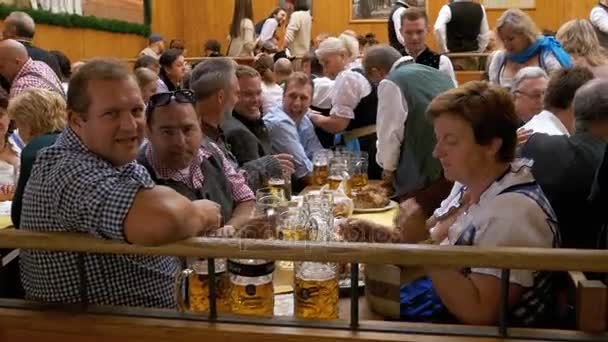 Пьяные люди за столом празднуют Октоберфест в большой пивной палатке. Бавария, Германия — стоковое видео