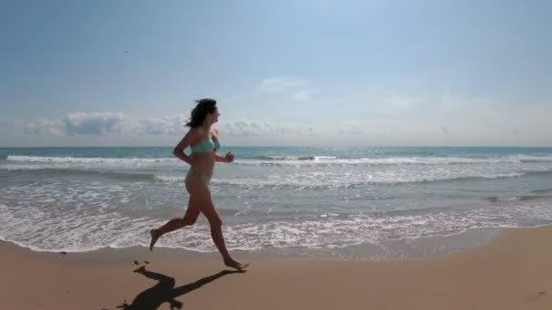 Die Kamera bewegt sich hinter der Frau, die in Zeitlupe am Strand entlang läuft — Stockvideo