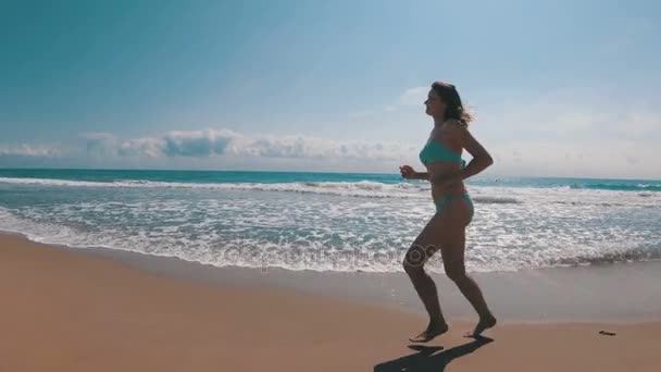 La cámara se mueve detrás de la mujer corriendo por la playa en cámara lenta — Vídeo de stock