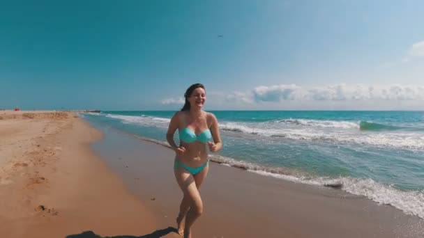 Młoda dziewczyna biegnie wzdłuż plaży na wybrzeżu morza w zwolnionym tempie — Wideo stockowe