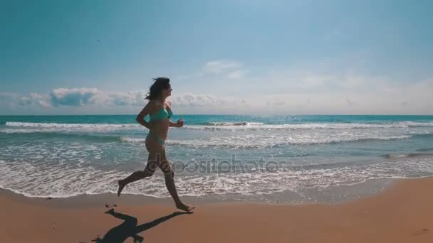 Chica joven corre a lo largo de la playa de la costa del mar en cámara lenta — Vídeo de stock