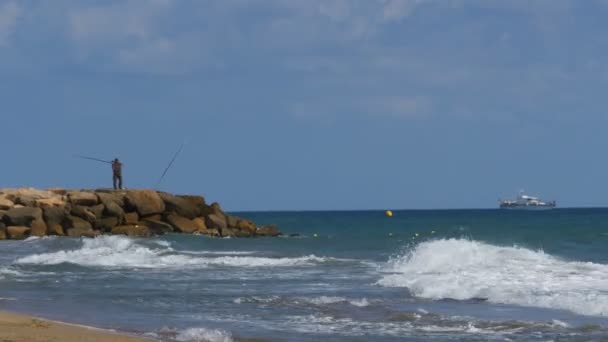 The fisherman throws a fishing pole in the sea, standing on a stony pier — Stock Video