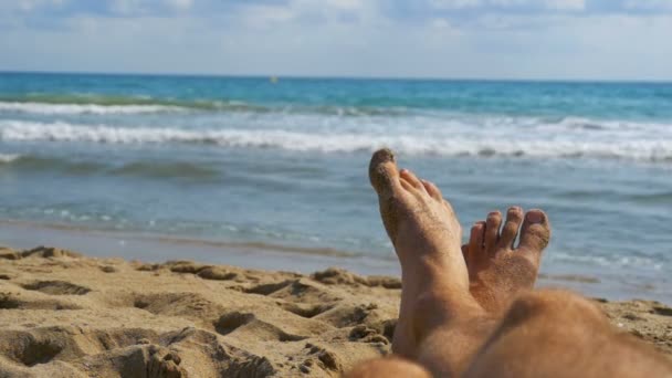 Beine eines Mannes, der am Strand in der Nähe des Meeres liegt, pov. Zeitlupe — Stockvideo