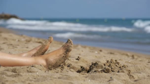 Gambe di donna sdraiato sulla spiaggia vicino al mare in slow motion — Video Stock
