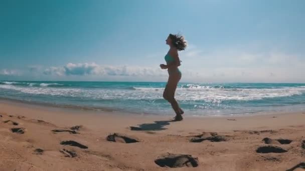 La cámara se mueve detrás de la mujer corriendo por la playa en cámara lenta — Vídeo de stock