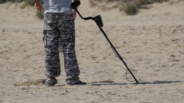 Man met een metaaldetector loopt langs een zandstrand aan de kust — Stockvideo