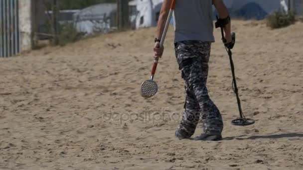 Homem com um detector de metais caminha ao longo de uma praia de areia no litoral — Vídeo de Stock