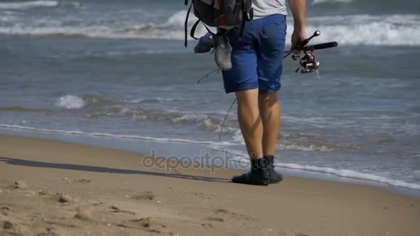 Nelayan dengan tongkat pancing dan ransel berjalan di sepanjang pantai pantai laut. Pergerakan Lambat — Stok Video