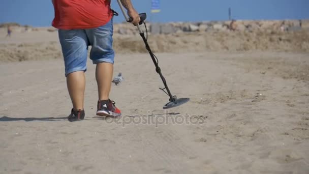 Człowiek z wykrywaczem metali idzie wzdłuż piaszczystej plaży nad brzegiem morza. Zwolnionym tempie — Wideo stockowe