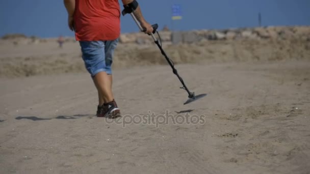El hombre con un detector de metales camina a lo largo de una playa de arena en la costa. Moción lenta — Vídeo de stock