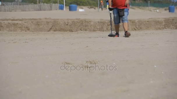 El hombre con un detector de metales camina a lo largo de una playa de arena en la costa. Moción lenta — Vídeo de stock