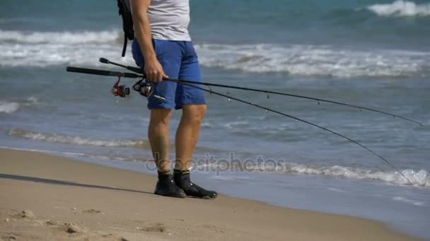 Balıkçı balıkçılık çubuklar ve bir sırt çantası ile deniz sahil plaj boyunca yürür. Ağır çekim — Stok video