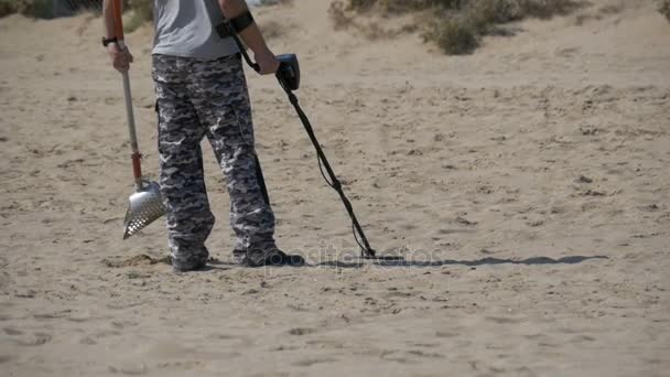 Homem com um detector de metais caminha ao longo de uma praia de areia no litoral. Movimento lento — Vídeo de Stock