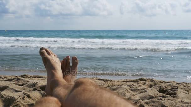 Πόδια του άνδρες ξαπλωμένοι στην παραλία κοντά στην θάλασσα, Pov. Αργή κίνηση — Αρχείο Βίντεο