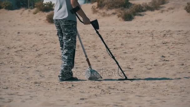 El hombre con un detector de metales camina a lo largo de una playa de arena en la costa. Moción lenta — Vídeos de Stock