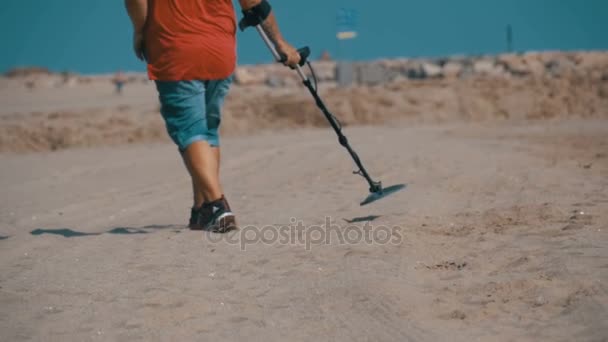 Άνθρωπος με έναν ανιχνευτή μετάλλων που περπατά κατά μήκος μια αμμώδης παραλία στην παραλία. Αργή κίνηση — Αρχείο Βίντεο