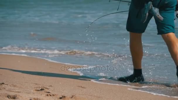 Pieds de pêcheur avec cannes à pêche et un sac à dos se promène le long de la plage de la côte de la mer. Mouvement lent — Video