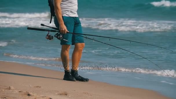 Pieds de pêcheur avec cannes à pêche et un sac à dos se promène le long de la plage de la côte de la mer. Mouvement lent — Video
