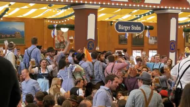 Tłum pijanych ludzi w strojach ludowych pić piwa i zabawy wewnątrz ogromny piwiarni. Bawaria, Niemcy — Wideo stockowe
