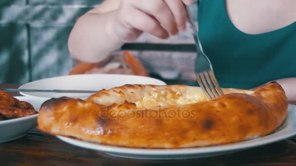 ジョージアン レストラン木製テーブルの上にフォークで Adjarian Khachapuri を食べる女。グルジア料理 — ストック動画