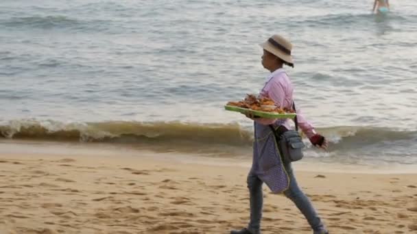 Mujer vendedora asiática lleva ventas de comida tropical en la playa. Pattaya, Tailandia — Vídeo de stock