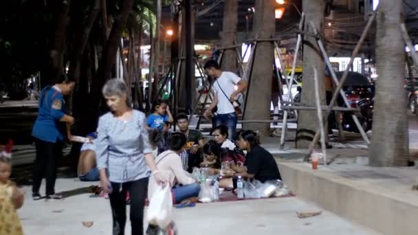 Asiatiques assis sur le trottoir manger de la nourriture sont dans la soirée près de la mer sur le remblai sous les palmiers — Video