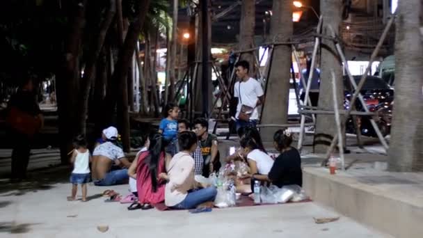 Asijské lidé sedí na chodníku jíst potraviny jsou večer u moře na nábřeží pod palmami — Stock video