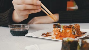Kadın suşi rulo yemek çubukları ile bir Japon restoranında yiyor.