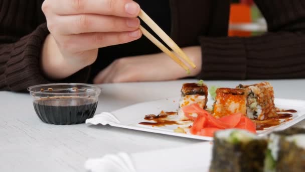 Chica come rollos de sushi con palillos en un restaurante japonés — Vídeos de Stock