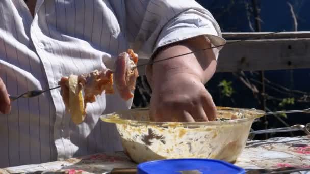 Fat Man pone la carne cruda marinada en un pincho para un shish kebab en la naturaleza . — Vídeo de stock