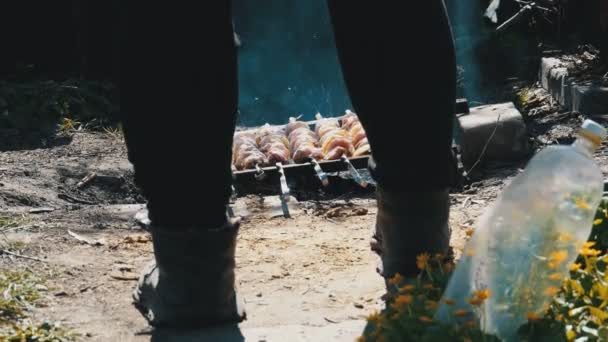 Una vista de las piernas de un hombre cocinando shish kebab en brochetas sobre un fuego en el campo en el pueblo — Vídeo de stock