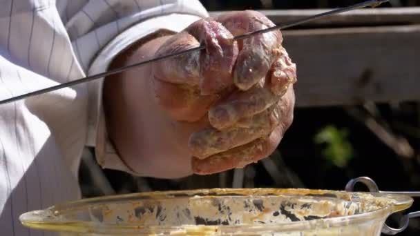 Толстяк кладет маринованное сырое мясо на шампур для шашлыка на природу . — стоковое видео