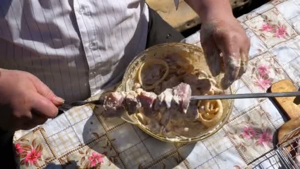 Dicke Mann legt das marinierte rohe Fleisch auf einen Spieß für einen Schaschlik auf die Natur. — Stockvideo