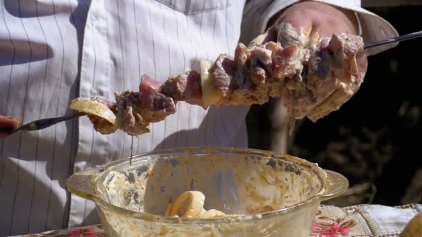 Dicke Mann legt das marinierte rohe Fleisch auf einen Spieß für einen Shish Kebab auf die Natur. Zeitlupe — Stockvideo