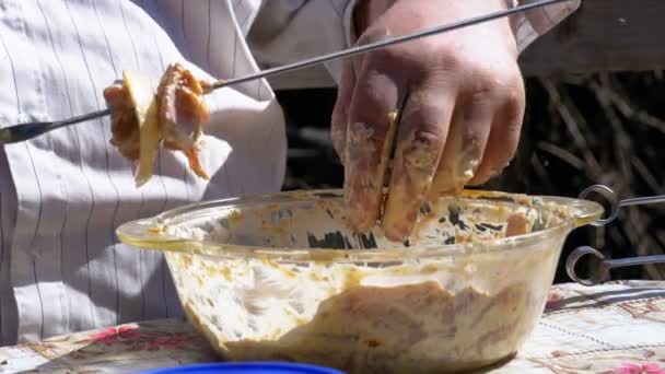 Жирний чоловік саджає мариновану сиру м'ясо на блюдце для шашлику на природі . — стокове відео
