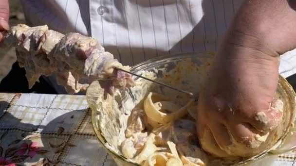 Gruby mężczyzna stawia marynowane mięso na szpikulec dla Shish Kebab na charakter. Zwolnionym tempie — Wideo stockowe