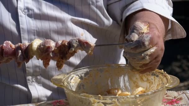 Dicke Mann legt das marinierte rohe Fleisch auf einen Spieß für einen Shish Kebab auf die Natur. Zeitlupe — Stockvideo