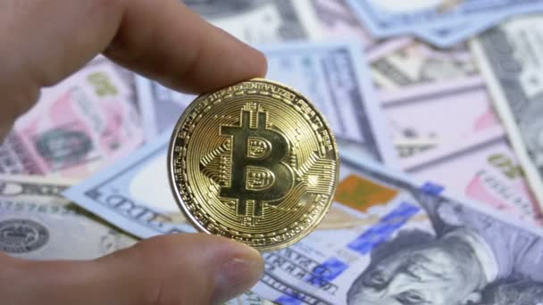Bir altın sikke Bitcoin, Btc dolar faturaları bir zemin üzerine parmak elinde tutan — Stok video
