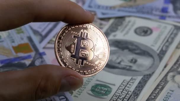 Hand in Fingers detém uma moeda de bronze Bitcoin, BTC em um fundo com contas de dólares — Vídeo de Stock