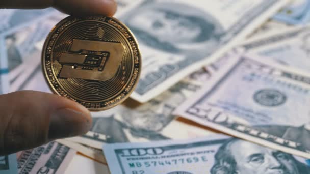 Hand in Fingers Holds a Gold Coin Dash on a Background with Bills of Dollars — Stock Video