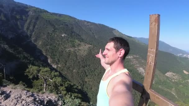 Vrolijke jongeman verhogen zijn handen hoog op de top van de grote rotsachtige berg met kruis — Stockvideo