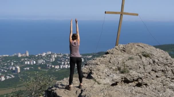 Una mujer practicando movimientos de yoga. Cliff top con la cruz . — Vídeos de Stock